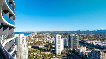 Um edifício alto com várias varandas, vista para uma paisagem costeira e um rio que corta a cidade.