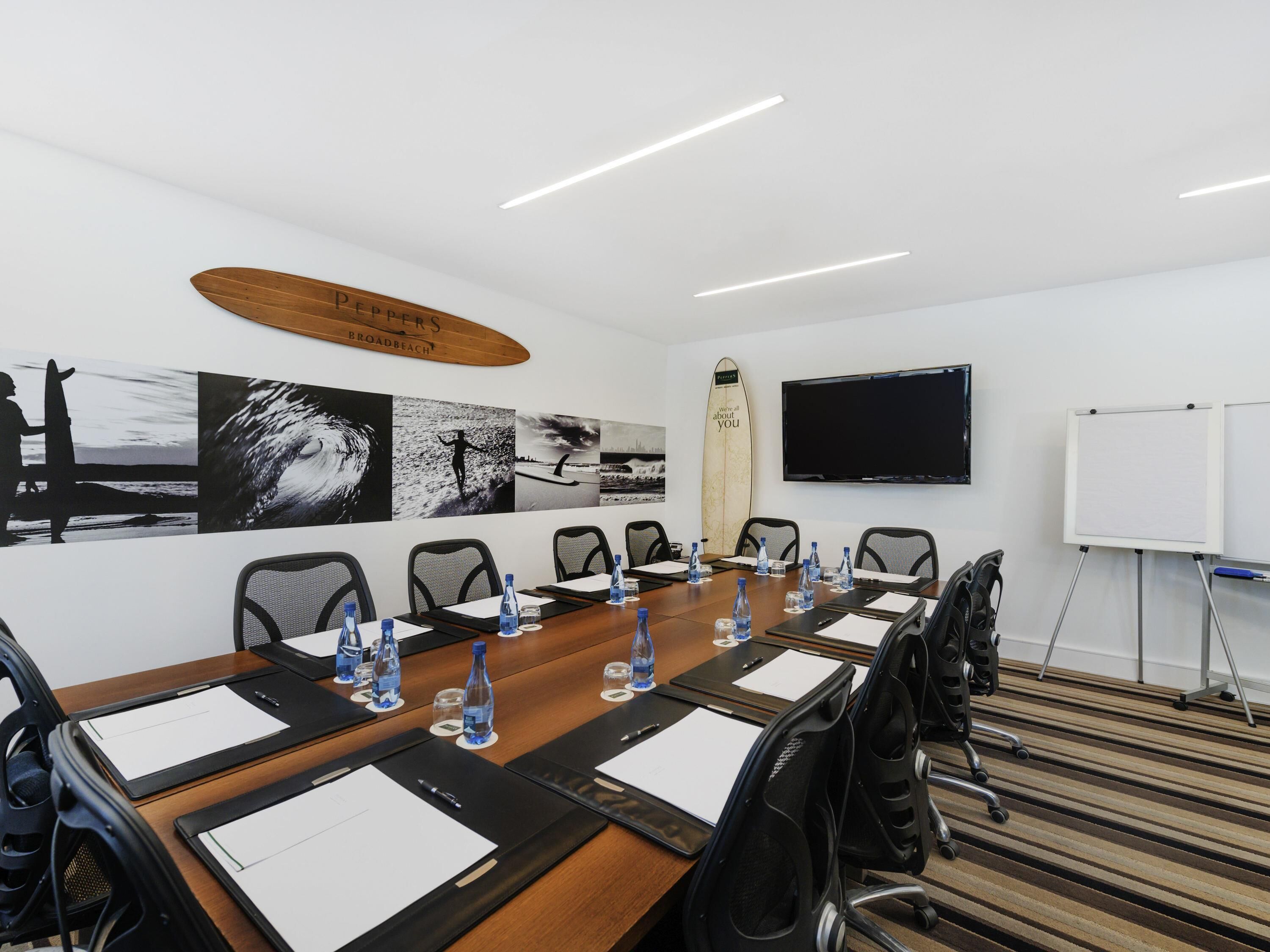 A conference room with a long table, chairs, water bottles, and a surfboard on the wall.