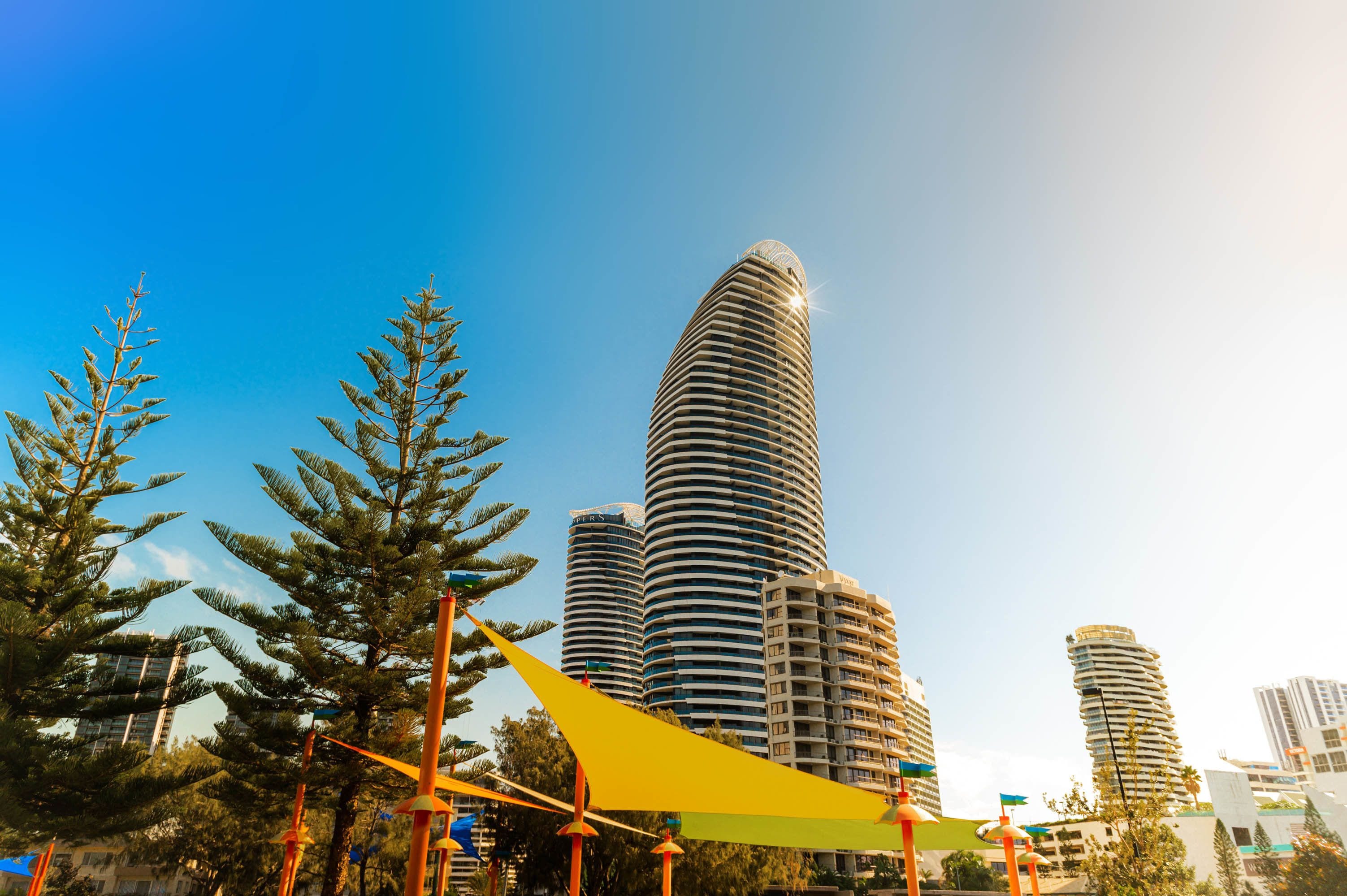 A modern high-rise building with a curved facade, surrounded by trees and a clear blue sky.