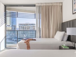 A hotel room with a large window, a bed, a nightstand, and a view of a cityscape.