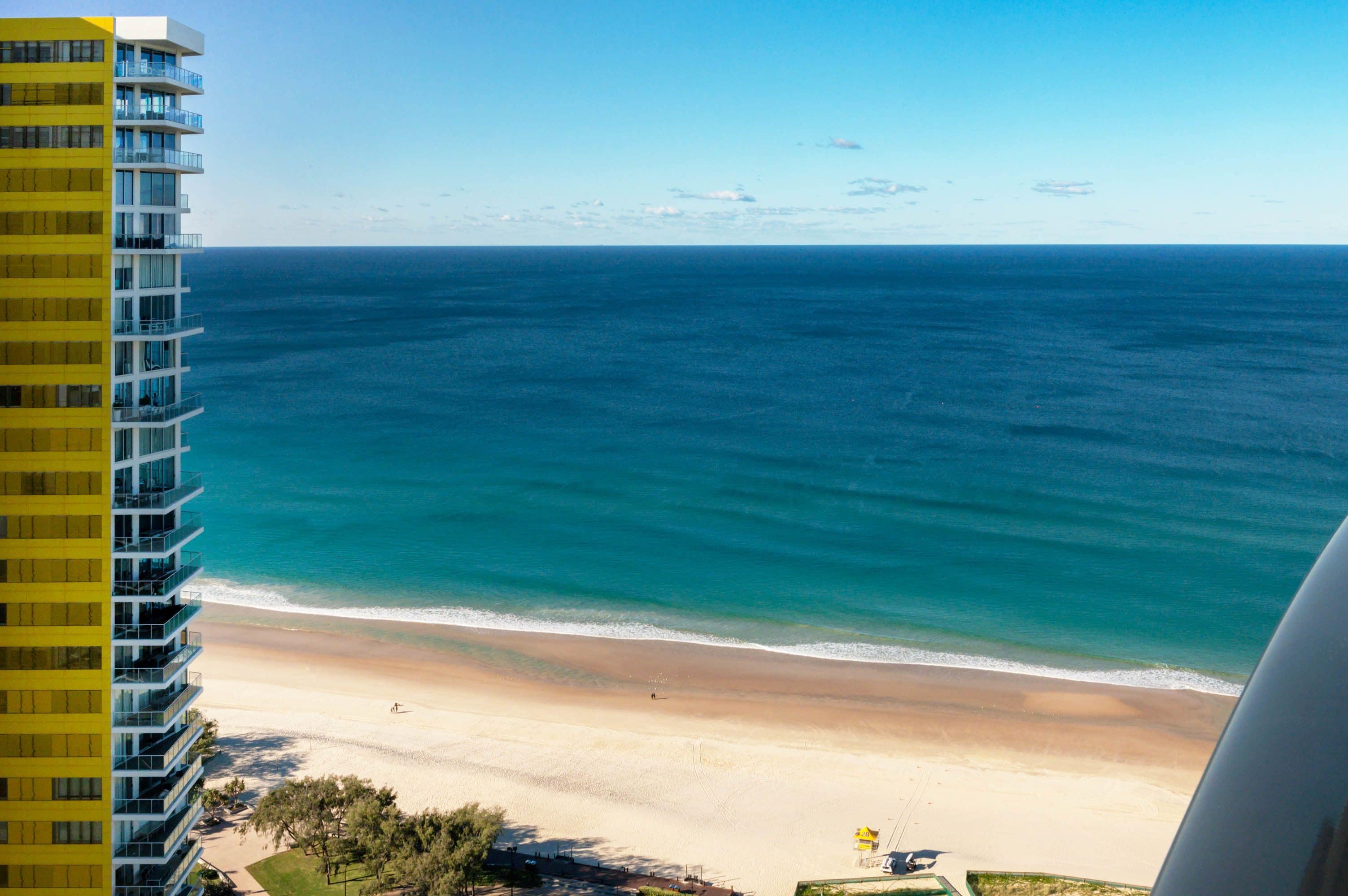 Ein Hochhaus-Hotel mit Blick auf einen Strand, das klare, blaue Wasser und einen Sandstrand zeigt.