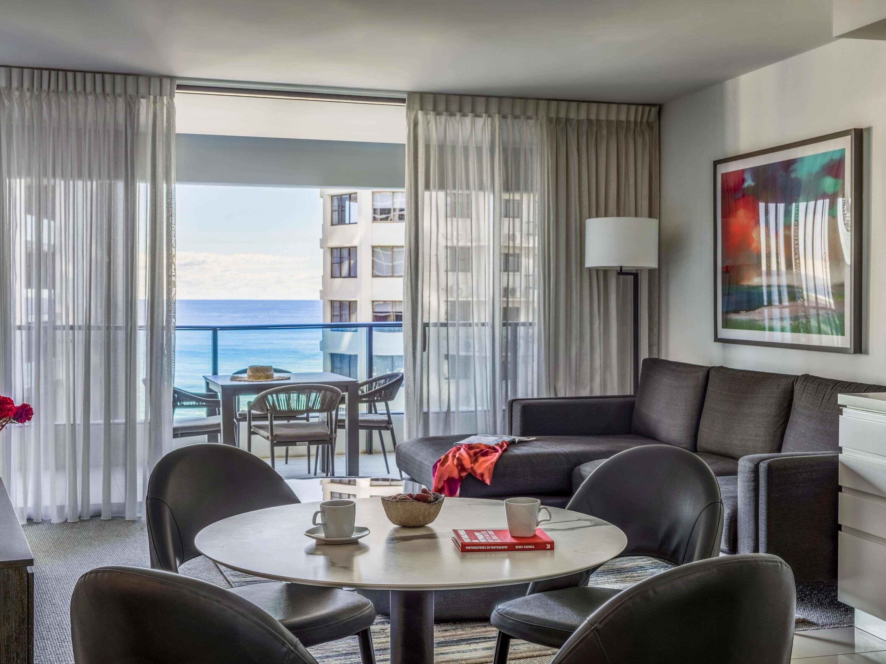 A modern hotel room with a balcony, a round dining table, and a sofa.