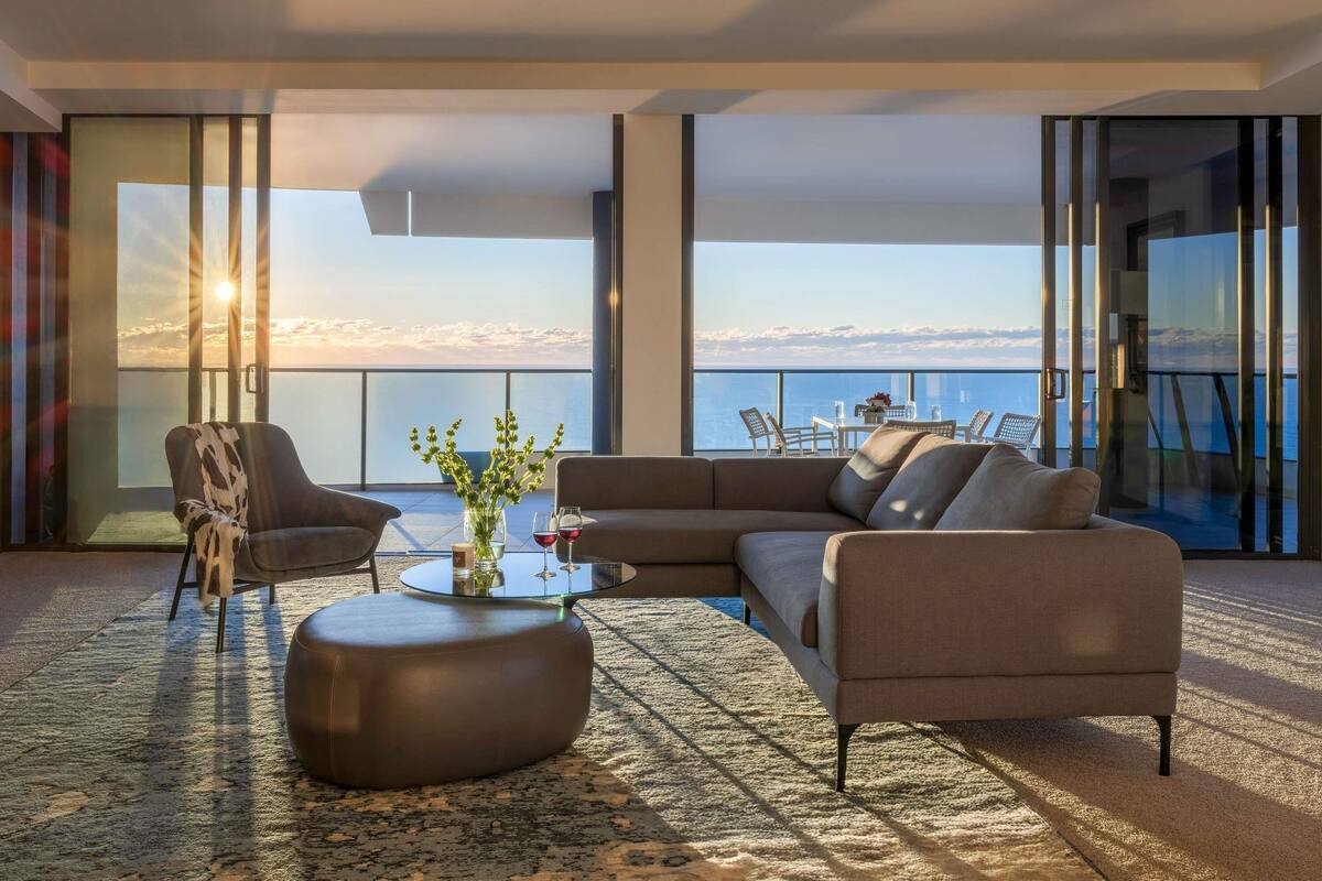 Una sala de estar moderna con sofá, sillas, una mesa de centro y vista al mar.