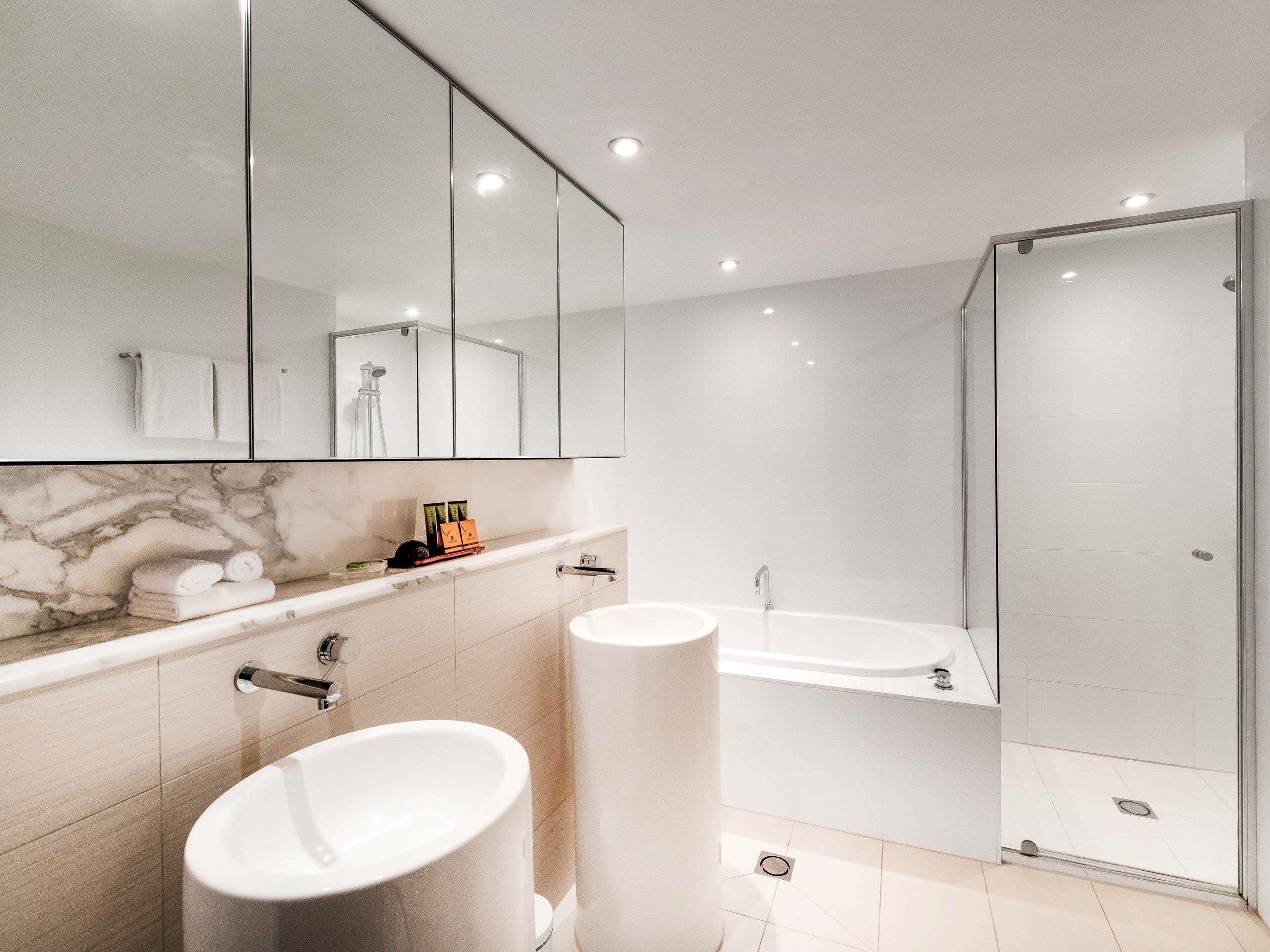 A modern bathroom with a marble vanity, a large mirror, a glass shower enclosure, and a toilet.