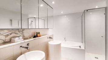A modern bathroom with a marble vanity, a large mirror, a glass shower enclosure, and a toilet.