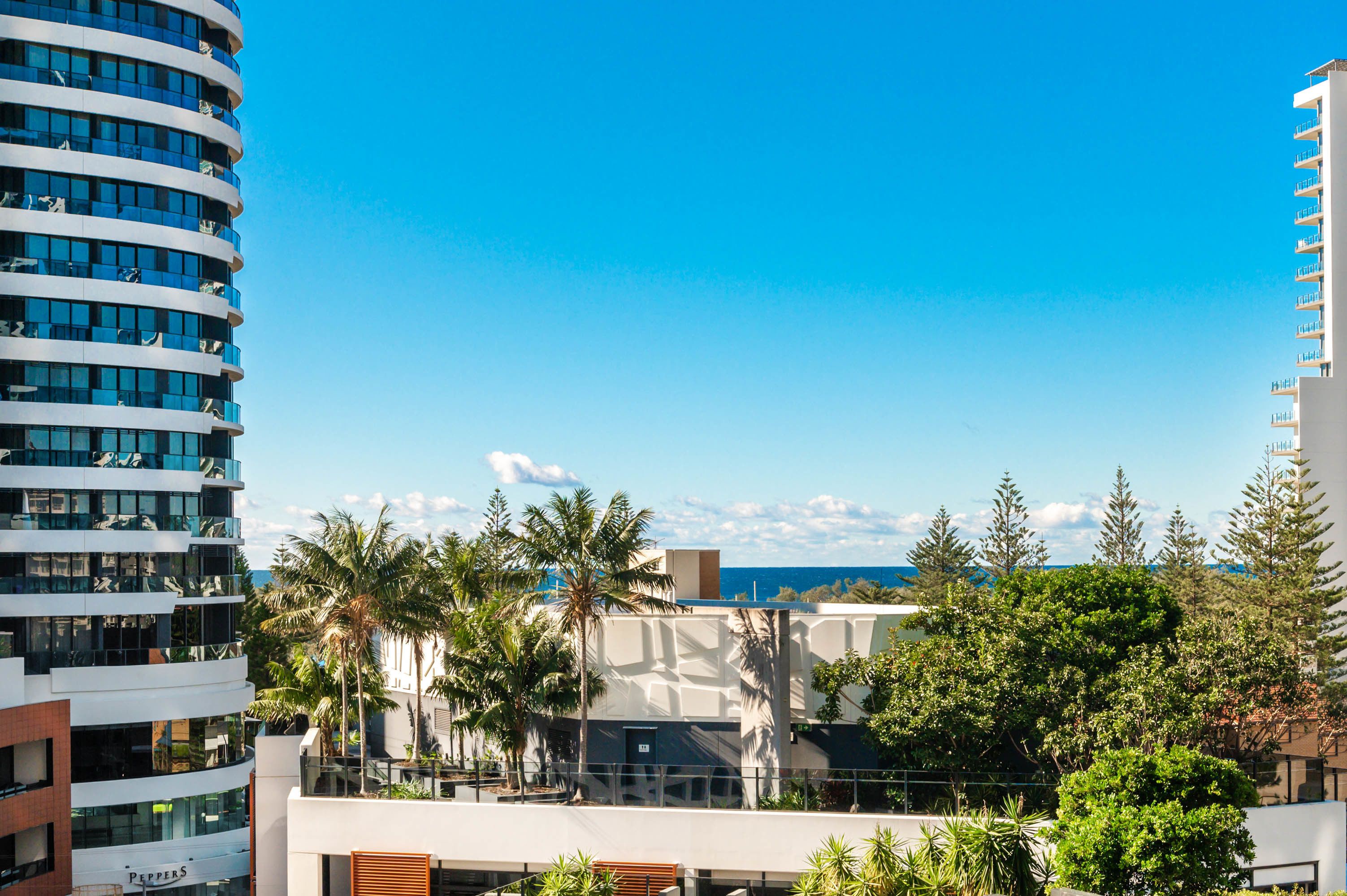 A modern hotel with a curved facade, multiple balconies, and a view of the ocean.