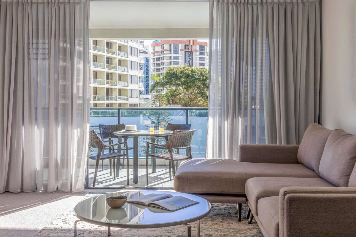 Una habitación de hotel moderna con balcón, sofá, una mesa redonda y vistas a la ciudad.