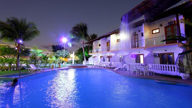 A swimming pool with lounge chairs and a building with balconies. - Benko's Praia Hotel (Porto Seguro)