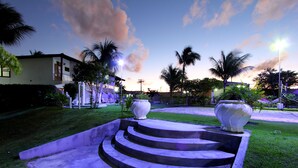 A landscaped garden with a concrete staircase leading to a decorative area, surrounded by palm trees and a building in the background. - Benko's Praia Hotel (Porto Seguro)