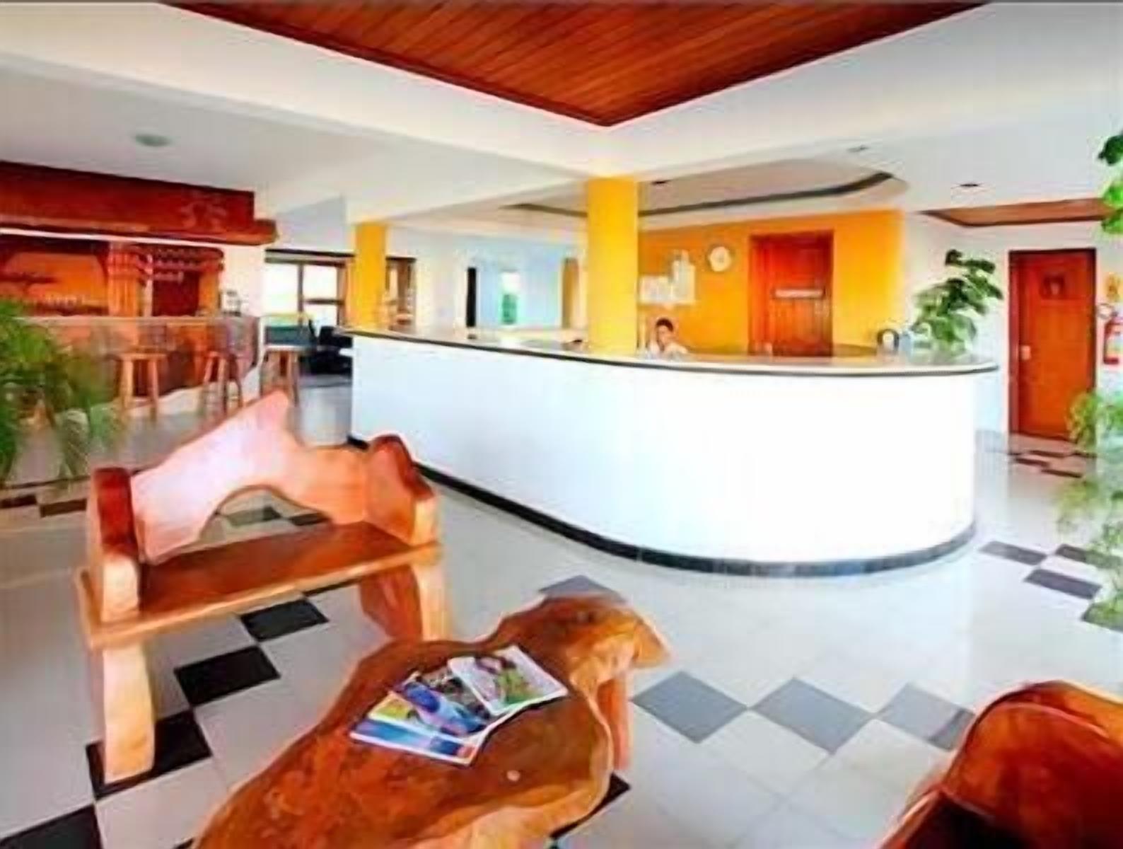 A hotel lobby with a reception desk, a check-in counter, a seating area with a wooden bench, and a tiled floor.