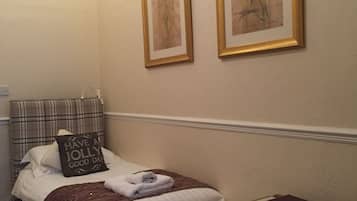A neatly arranged bedroom with a bed, a bedside table with a book and a remote, and two framed floral paintings on the wall.