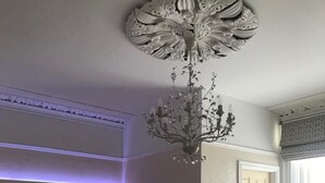 Een slaapkamer met een groot bed, een kroonluchter, een dressoir en een deur naar een andere kamer.