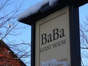 A sign for 'BaBa Guest House' with a snow-covered roof and bare trees in the background. - Ba Ba Guest House (Chester)