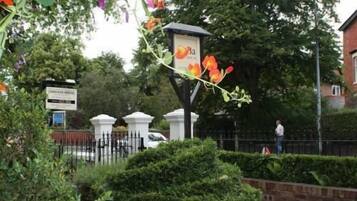 A gated entrance with a signboard, a white car, and a person standing by the gate.