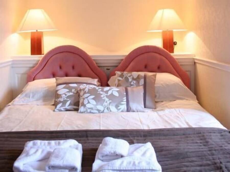 Un lit avec une tête de lit rose, une literie blanche et deux lampes de chaque côté.