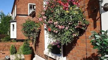 Traditional brick house with a charming garden featuring a hanging flower basket, potted plants, and a cozy outdoor seating area.