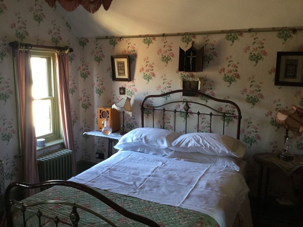 Een slaapkamer met bloemenbehang, een houten bedframe, een nachtkastje met een lamp en een raam met gordijnen.