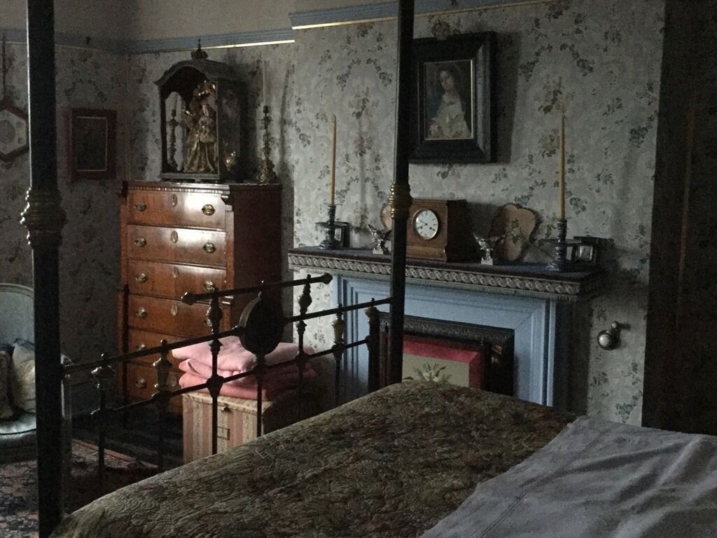 Une chambre à coucher avec un lit à baldaquin, une commode en bois, une horloge et un tableau encadré accroché au mur.