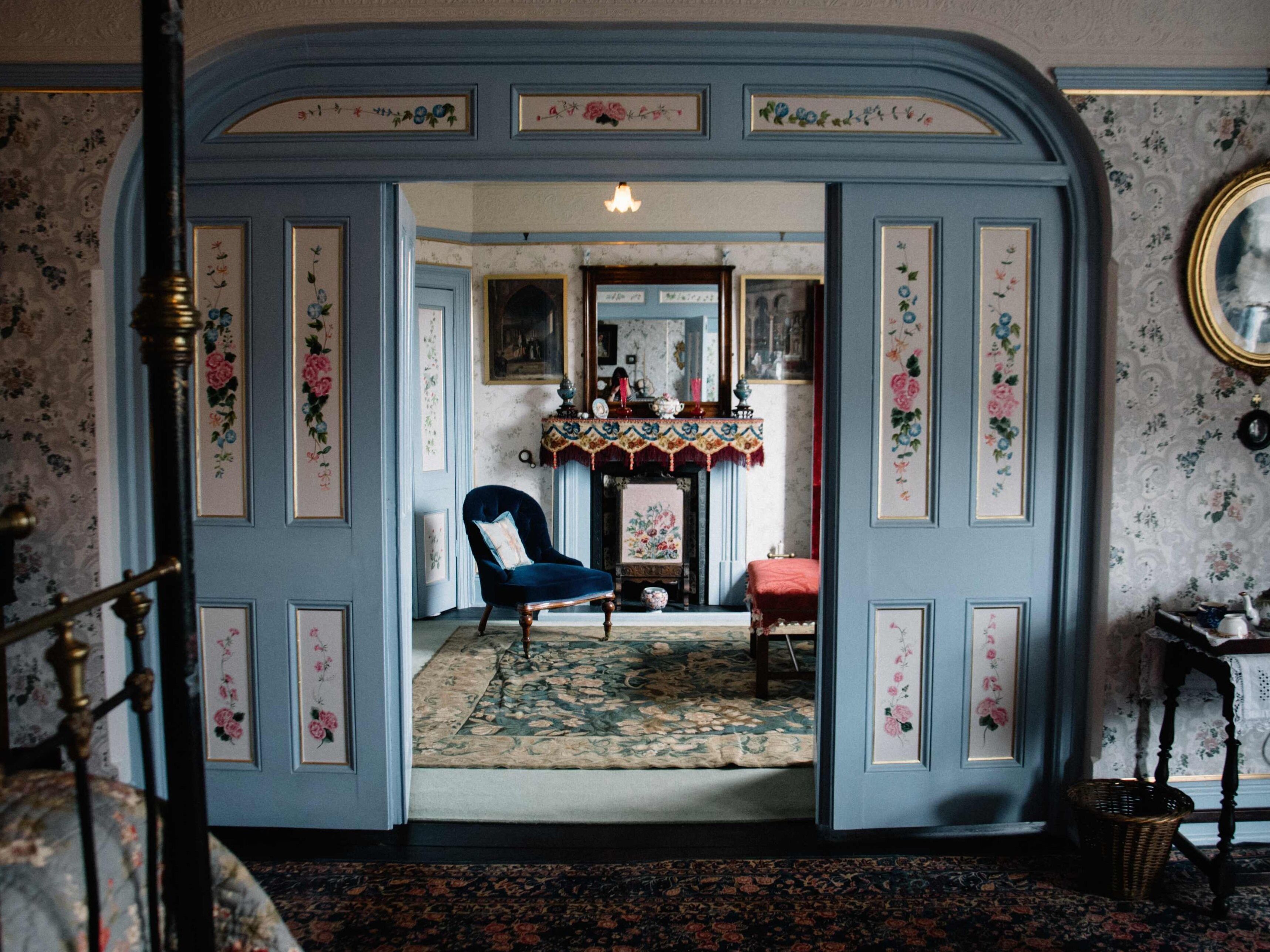 Una habitación con una puerta azul, un sillón azul, un banco rojo y una alfombra estampada.
