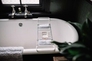 Une salle de bain avec une baignoire blanche, un porte-serviettes sur lequel est pliée une serviette, et une fenêtre ornée de rideaux à motifs.