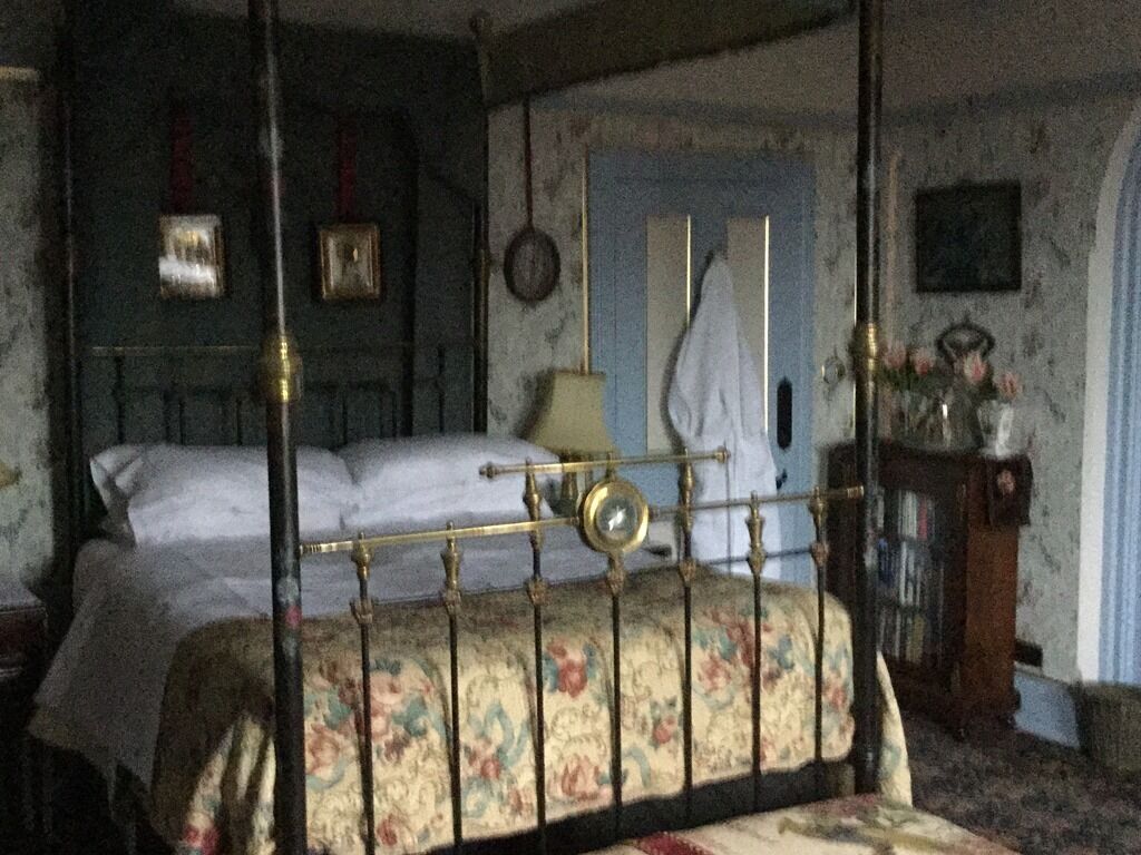 A bedroom with a four-poster bed, a nightstand, a dresser, and a door with a towel hanging on it.