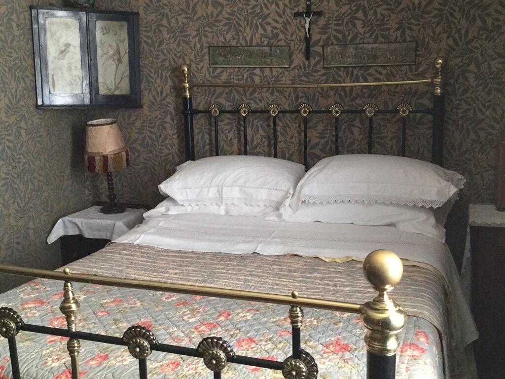 Uma cama com colcha estampada em flor, cabeceira de latão e mesa de cabeceira com abajur.