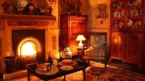 A warmly lit room with a fireplace, a table with tea set, and a cabinet with dishes.