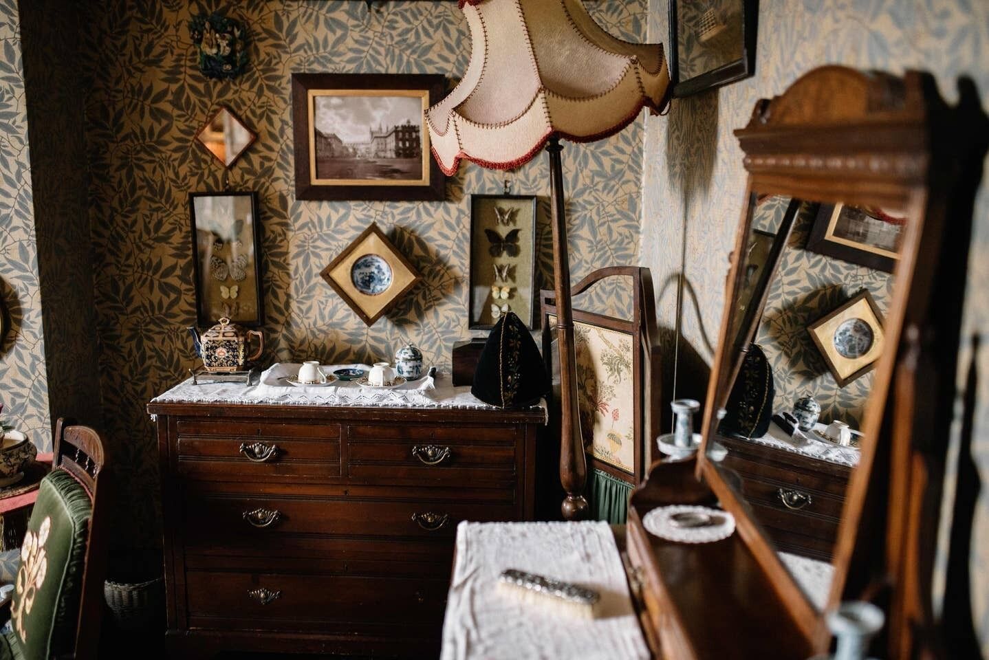 A vintage room with a wooden dresser, a mirror, and various framed pictures on the wall.