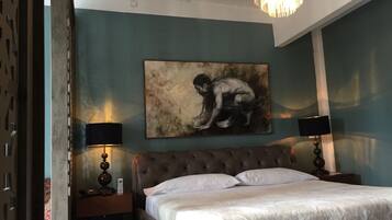 Une chambre à coucher avec un grand lit, deux tables de chevet avec des lampes, un tableau au mur et un lustre.