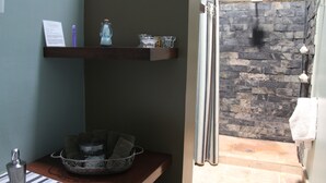 A bathroom with a stone wall, a shower area, and a shelf with toiletries. - La Casa del Atrio (Querétaro)