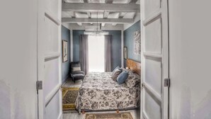 A bedroom with a bed, a chair, a chandelier, and a view of the outside. - La Casa del Atrio (Querétaro)