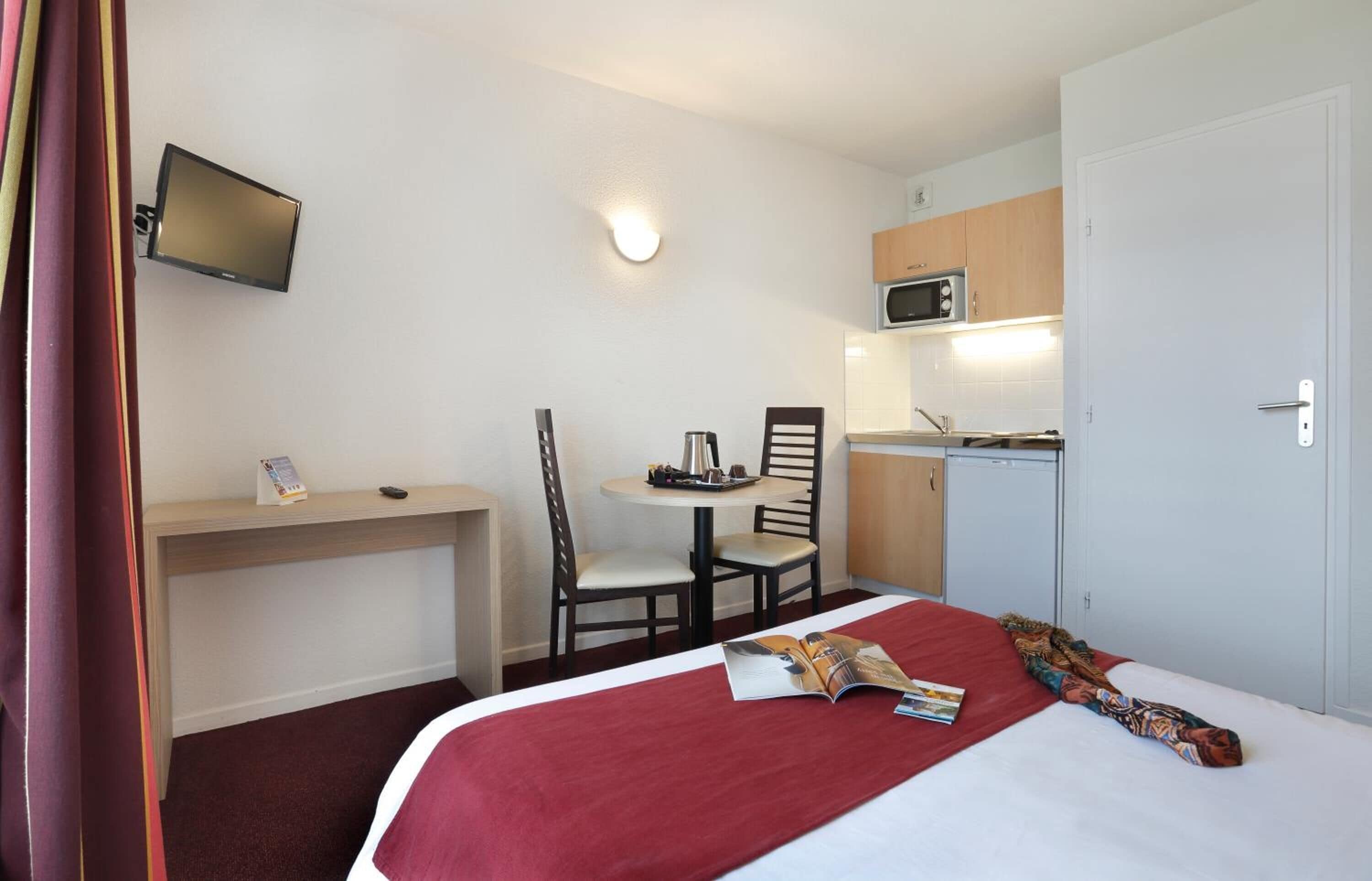 Habitación de hotel con cama, escritorio, silla, mesita, microondas y televisor montado en la pared.