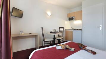 Habitación de hotel con cama, escritorio, silla, mesita, microondas y televisor montado en la pared.
