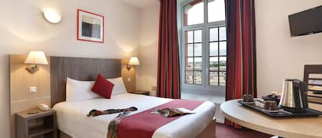 Una habitación de hotel con cama, mesitas de noche, un escritorio con silla, televisión y ventana con cortinas.
