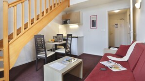 Un espacio habitable pequeño con una escalera de madera, una kitchenette, un comedor y un sofá rojo.