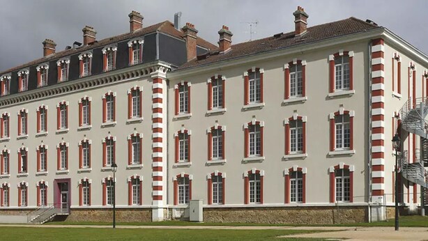 Un edificio grande e histórico con fachada simétrica, múltiples ventanas y una escalera central.