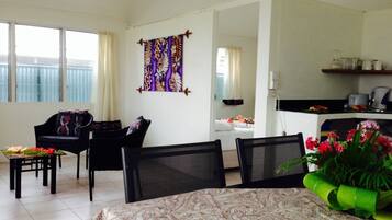 A living room with a sofa, chairs, a dining table, and a kitchen area with a counter and appliances.