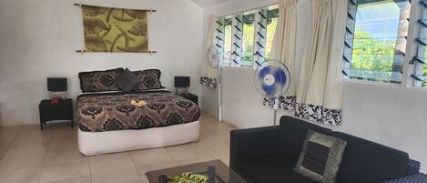 A bedroom with a bed, bedside tables, a fan, a sofa, and a window with curtains.