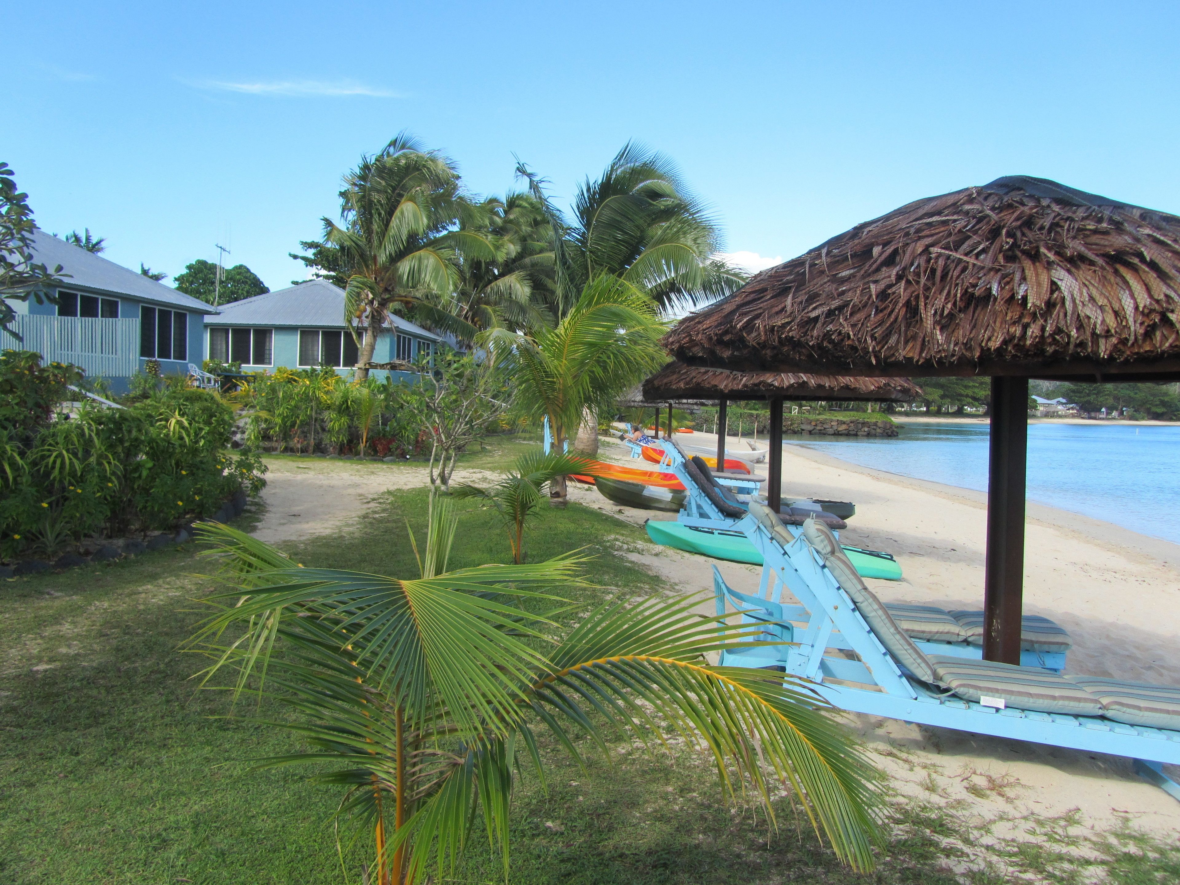 A beachside resort with a thatched-roof gazebo, palm trees, and a row of colorful paddle boats.