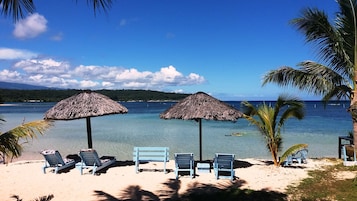 A beach with thatched umbrellas, lounge chairs, and clear blue water.