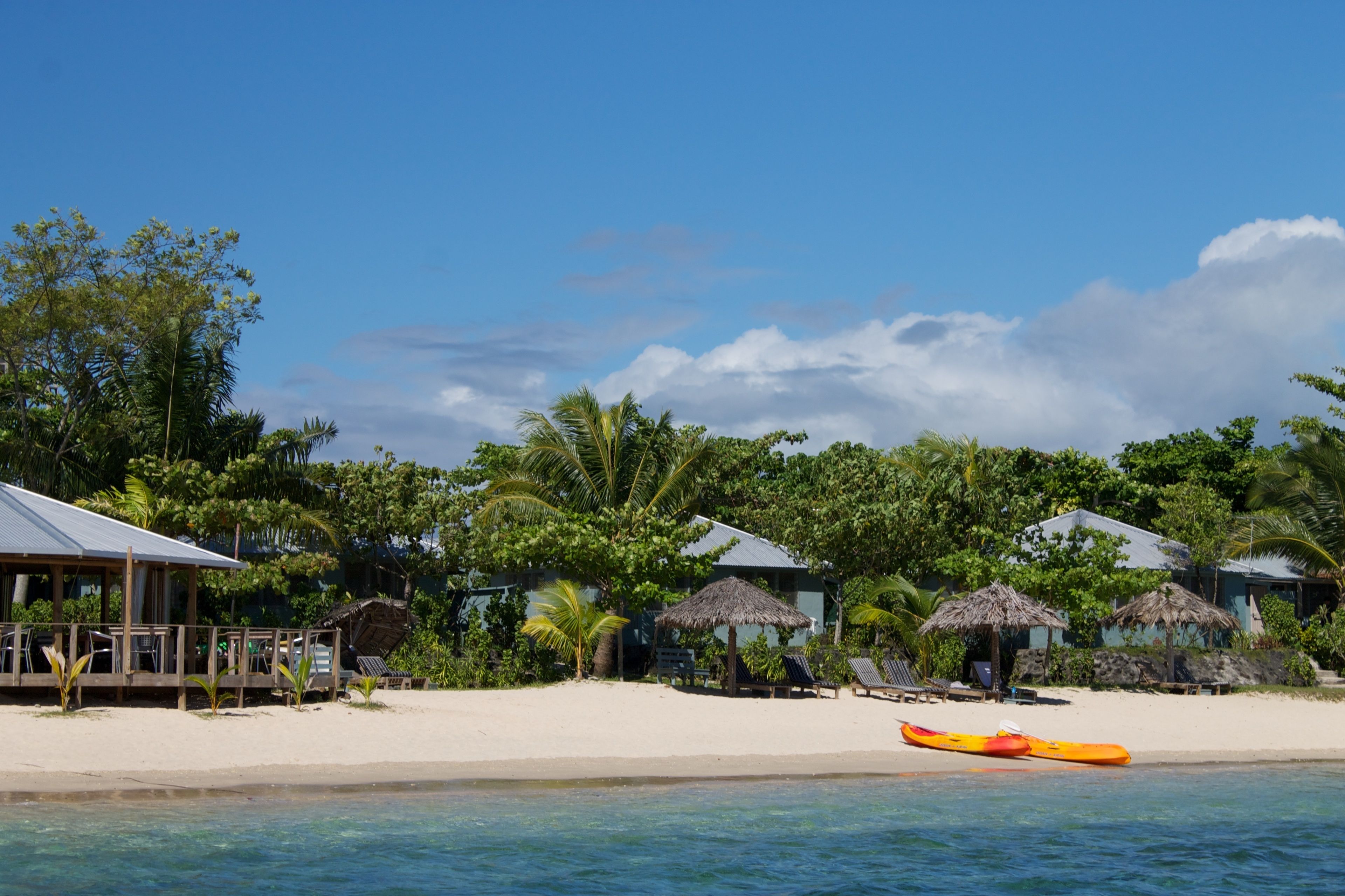A beachside resort with thatched-roof huts, lounge chairs, and a clear view of the ocean.