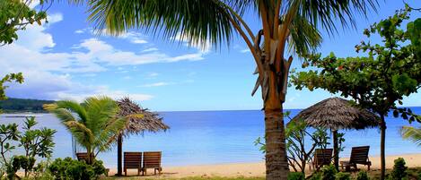 A beach with thatched umbrellas, wooden chairs, and a bench.
