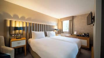 Ett hotellrum med två sängar, ett skrivbord, en stol, en TV och ett fönster med gardiner.