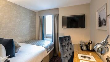 A hotel room with a bed, a desk, a chair, a television, and a window with curtains.