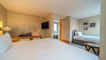 Una habitación de hotel con una cama grande, una mesita de noche con lámpara, un televisor montado en la pared y una pequeña mesa con una silla.