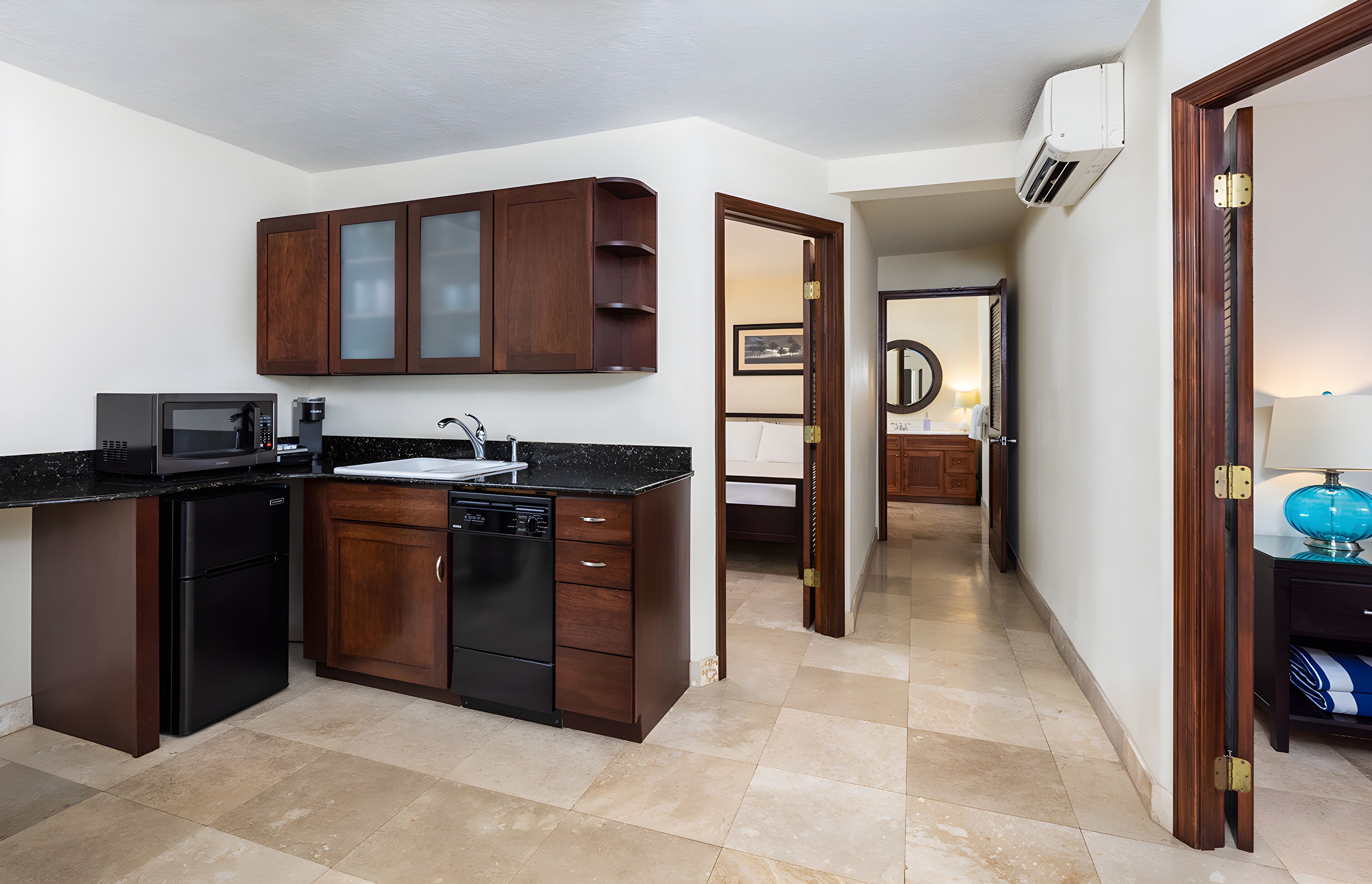 A compact kitchen with dark wood cabinets, a black refrigerator, a microwave, and a dishwasher.