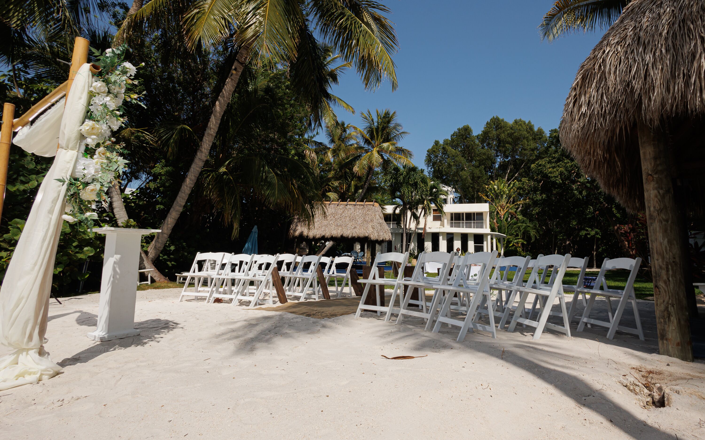 Decoração de casamento na praia com cadeiras e arco brancos.
