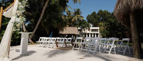 Decoración de boda en la playa, con sillas blancas y un arco blanco.