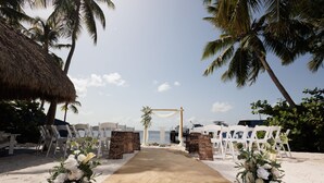 A beach wedding setup with a sandy aisle, white chairs, and floral decorations. - Azul del Mar (Key Largo)