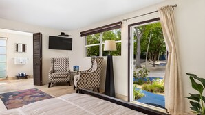 A hotel room with a large bed, two patterned armchairs, a TV, and a view of the outdoor area. - Azul del Mar (Key Largo)